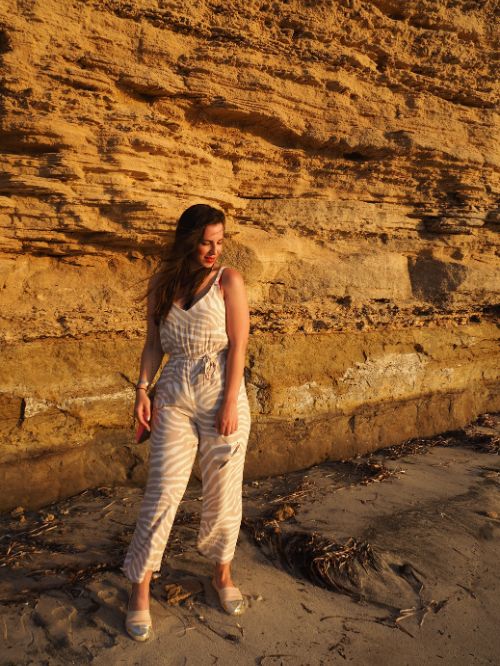 Gina Bley standing in front of a cliff in the golden sunset light wearing a light beige jumpsuit