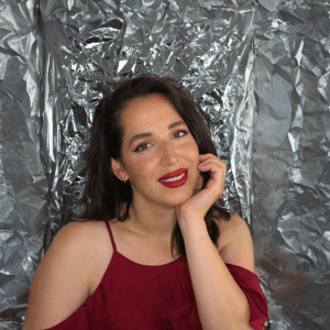 Gina Bley in front of a aluminium backdrop, dressed in a red flowy top, wearing red lipstick for the Pinterest section