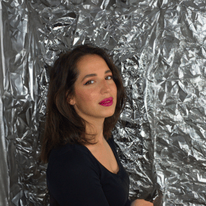 Gina Bley in front of a aluminium backdrop, dressed in a black longsleeved top, wearing pink lipstick for the TikTok section