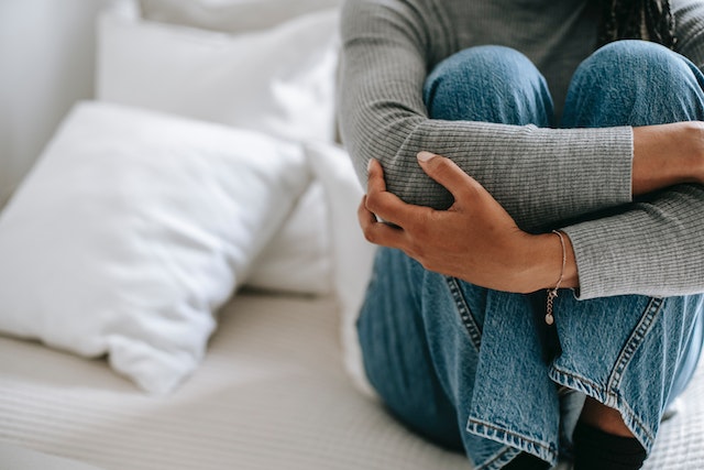 Image for the article "Overcoming Limiting Beliefs" shows a woman dressed in a grey longsleeved top and denim jeans holding her knees in self-doubt