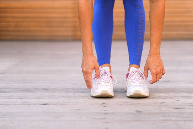 Image for the article "Overcoming Limiting Beliefs" shows a woman dressed in blue leggings and white running shoes stretching for her big run