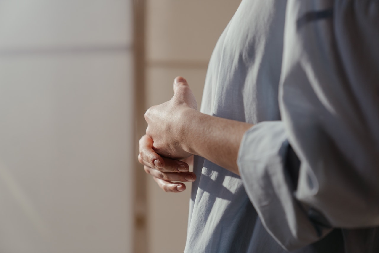 Image for the article "Overcoming Limiting Beliefs" shows a woman dressed in a loose white shirt holding her own hands n self-doubt