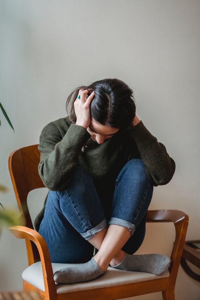 Image for the article "Overcoming Limiting Beliefs" shows a woman dressed in a dark longsleeved top and denim jeans scrunching her hair in negative self-talk