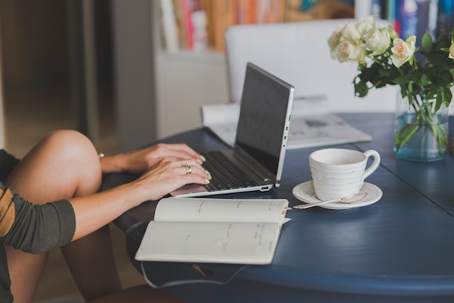 Image for the article "The Power of Journaling for Personal Insight" shows a woman sitting at a table working on a laptop with a journal and a coffee next to her