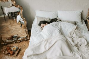 Image for the article "Why Sleep is the Foundation of Change" shows a bed with white linen and a woman sleeping in it